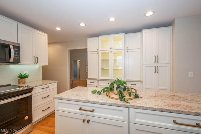 kitchen featuring appliances with stainless steel finishes, white cabinetry, backsplash, and light stone countertops