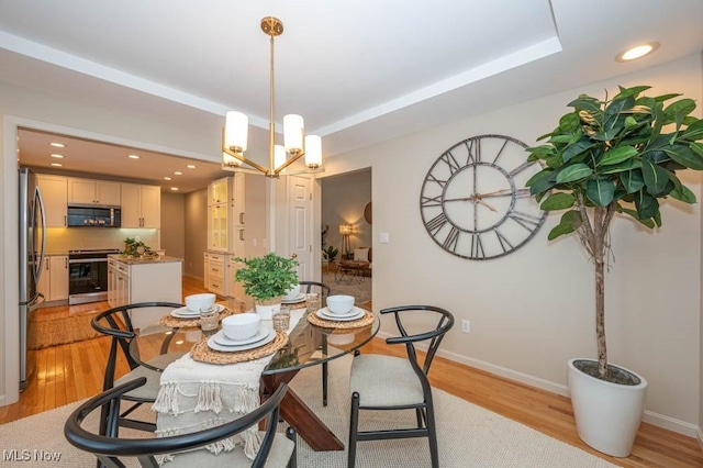 dining space with light wood-type flooring, a chandelier, and a tray ceiling