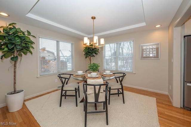 dining space with a chandelier, a tray ceiling, and light wood-type flooring