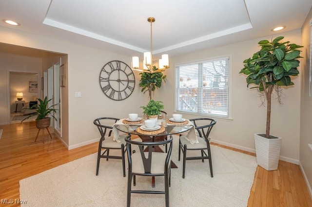 dining area featuring a chandelier, light wood-type flooring, and a tray ceiling