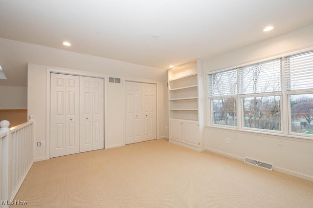 unfurnished bedroom featuring two closets and light colored carpet