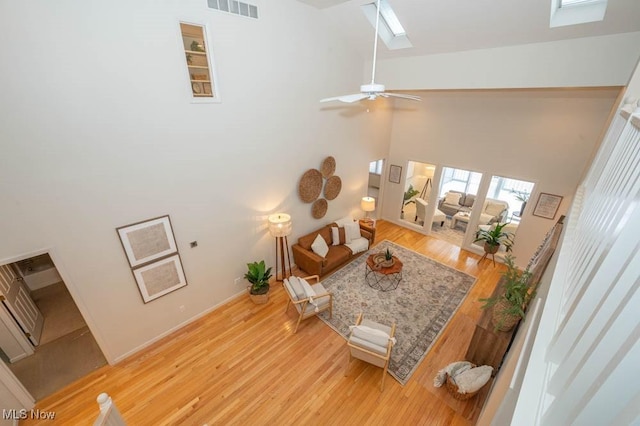 living room featuring ceiling fan, a skylight, a towering ceiling, and light wood-type flooring