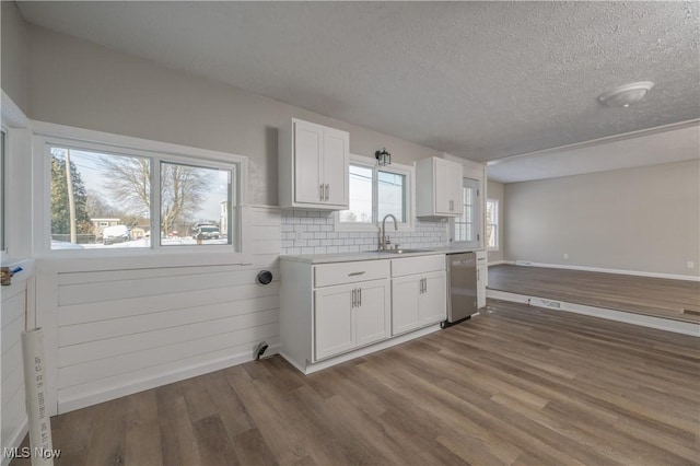 kitchen featuring dark wood-type flooring, sink, white cabinetry, stainless steel dishwasher, and tasteful backsplash