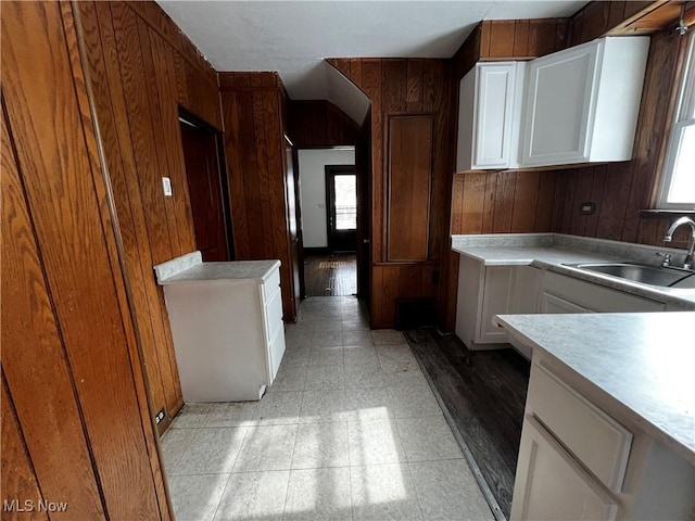 kitchen with white cabinetry, sink, wood walls, and a wealth of natural light