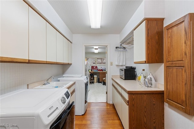 clothes washing area featuring separate washer and dryer, light hardwood / wood-style flooring, and sink