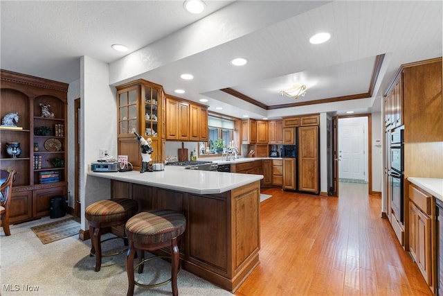 kitchen featuring kitchen peninsula, a breakfast bar, a tray ceiling, ornamental molding, and sink