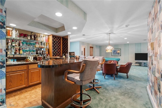 bar with light colored carpet, a tray ceiling, and pendant lighting