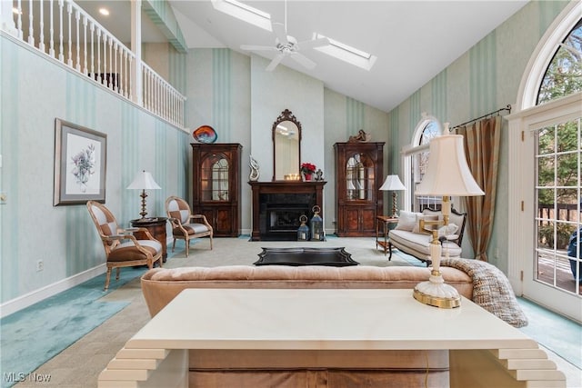 carpeted living room with ceiling fan, a skylight, and high vaulted ceiling