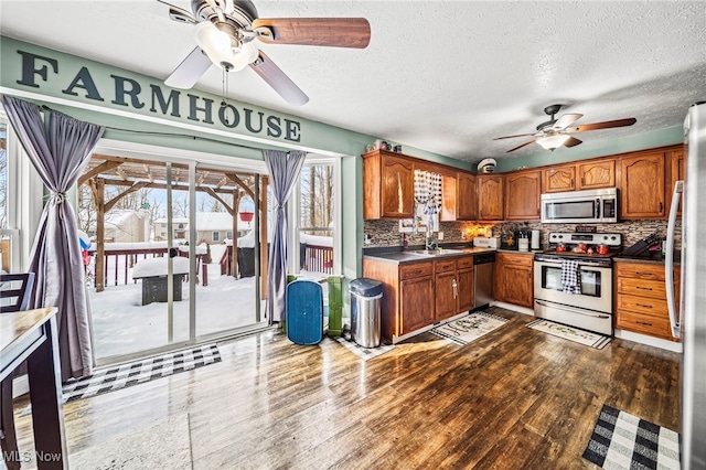 kitchen with dark wood finished floors, appliances with stainless steel finishes, brown cabinetry, a ceiling fan, and a sink