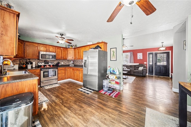 kitchen with dark countertops, stainless steel appliances, ceiling fan, and a sink