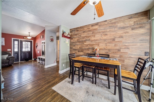 dining area with wood finished floors, wood walls, baseboards, ceiling fan, and vaulted ceiling