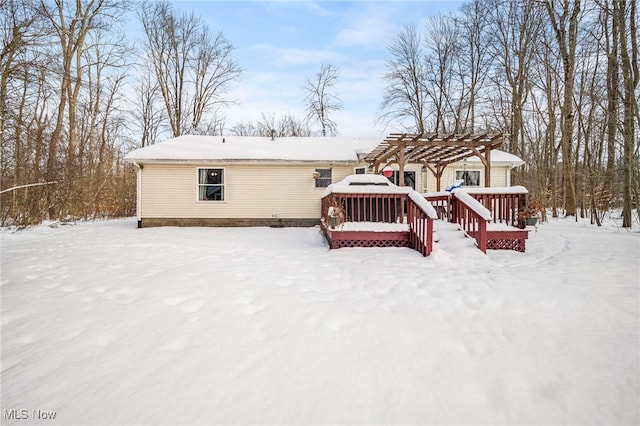 snow covered back of property with a pergola and a wooden deck