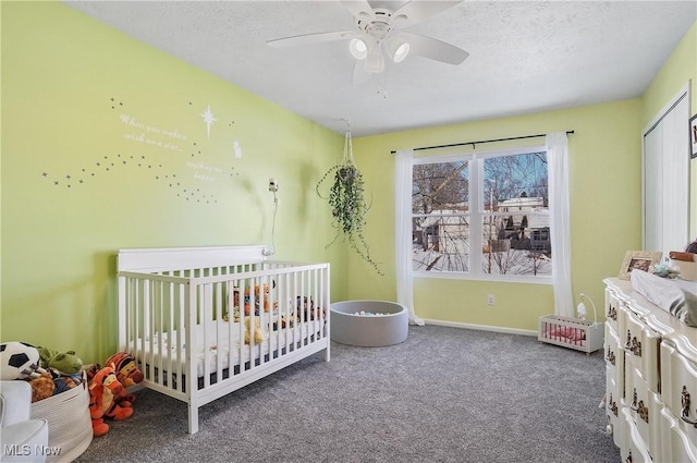 carpeted bedroom featuring a textured ceiling, ceiling fan, a crib, and a closet