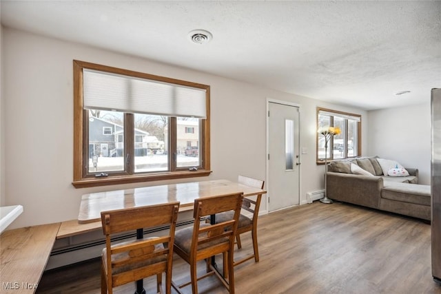 dining area featuring a textured ceiling, light hardwood / wood-style flooring, and a baseboard radiator