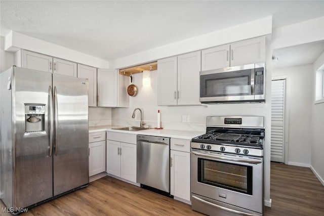 kitchen with sink, stainless steel appliances, white cabinetry, and hardwood / wood-style flooring