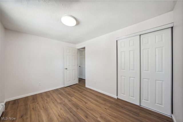 unfurnished bedroom with a baseboard heating unit, a closet, and dark hardwood / wood-style floors