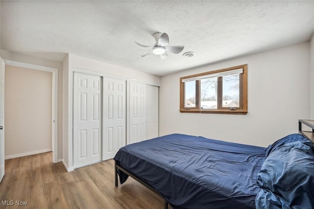 bedroom with ceiling fan, multiple closets, a textured ceiling, and wood-type flooring