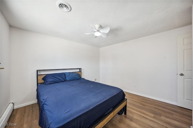 bedroom with baseboard heating, ceiling fan, and dark hardwood / wood-style floors