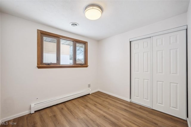 unfurnished bedroom featuring a closet, a baseboard heating unit, and hardwood / wood-style floors