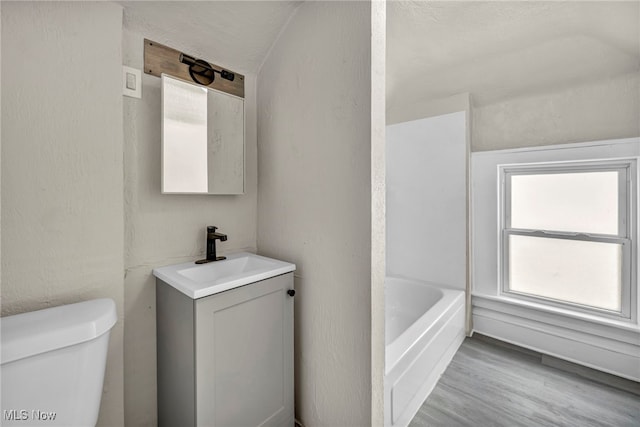 bathroom with toilet, hardwood / wood-style flooring, a bath, and vanity