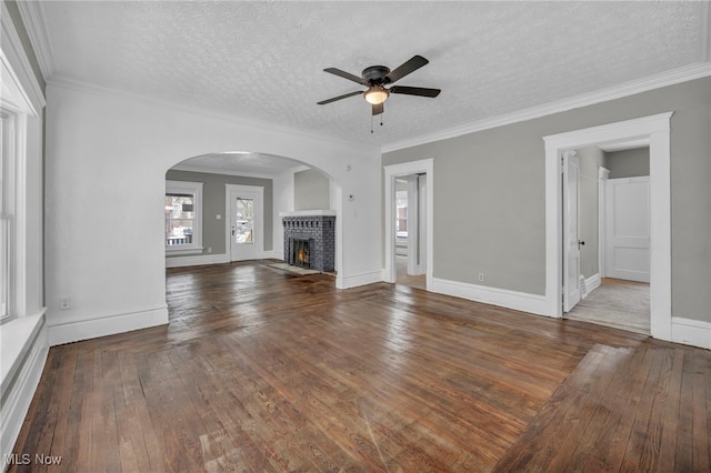 unfurnished living room featuring a textured ceiling, ceiling fan, ornamental molding, wood-type flooring, and a brick fireplace