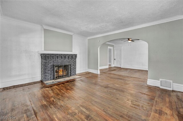 unfurnished living room with a textured ceiling, a brick fireplace, ornamental molding, ceiling fan, and wood-type flooring