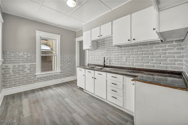 kitchen with sink, light hardwood / wood-style flooring, white cabinetry, and brick wall