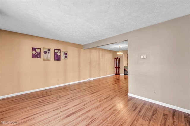 spare room featuring an inviting chandelier, a textured ceiling, and hardwood / wood-style floors