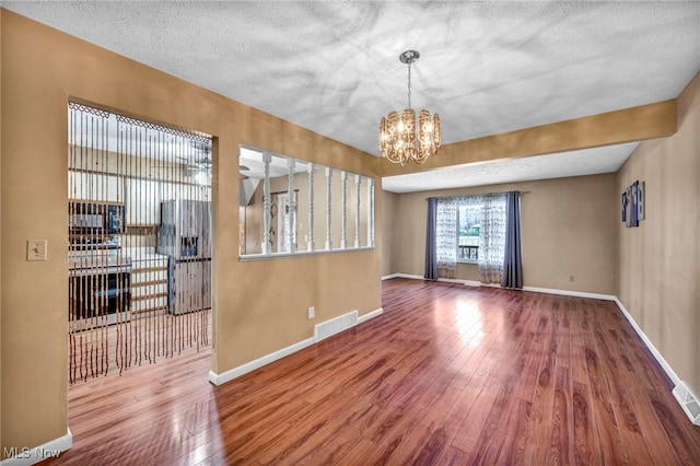 unfurnished living room featuring a notable chandelier, a textured ceiling, and wood-type flooring