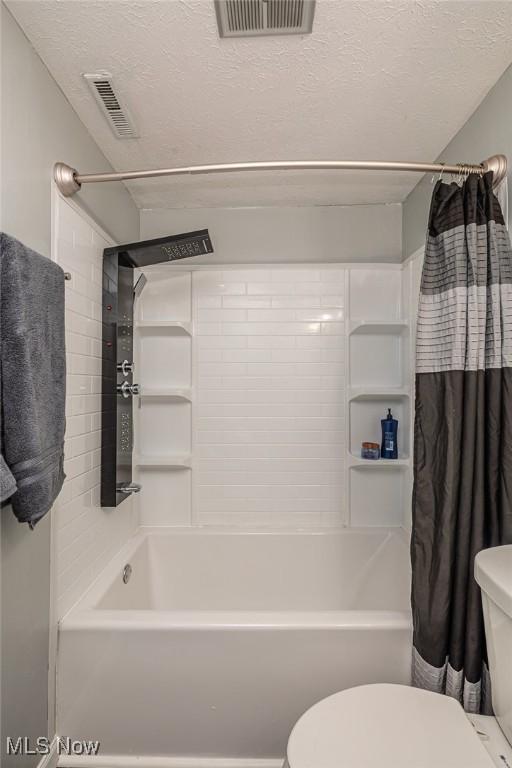 bathroom featuring a textured ceiling, shower / bath combination with curtain, and toilet