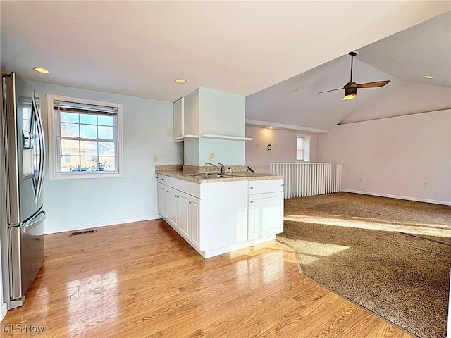 kitchen featuring vaulted ceiling, stainless steel fridge with ice dispenser, light wood-type flooring, kitchen peninsula, and white cabinetry