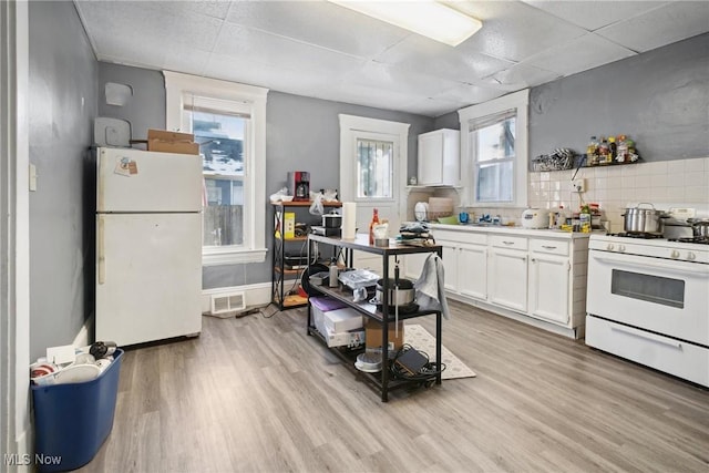 kitchen with white appliances, light wood-type flooring, white cabinets, and a wealth of natural light