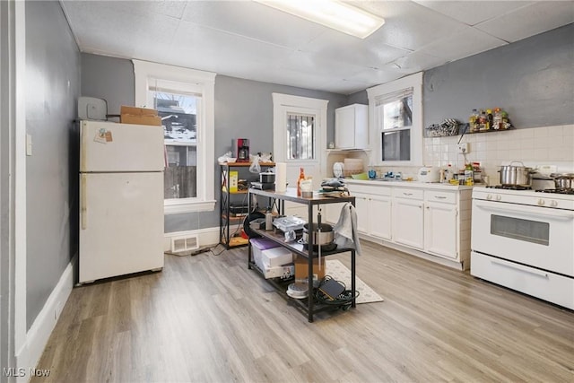 kitchen featuring white appliances, light wood-type flooring, a drop ceiling, white cabinets, and tasteful backsplash