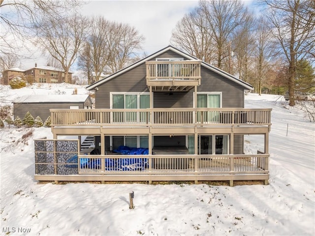 snow covered back of property with a wooden deck and a balcony