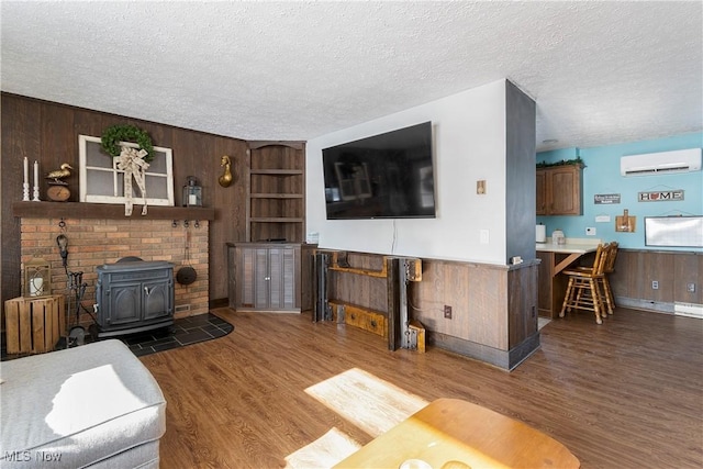 living room with wood walls, an AC wall unit, dark wood-type flooring, a wood stove, and a textured ceiling