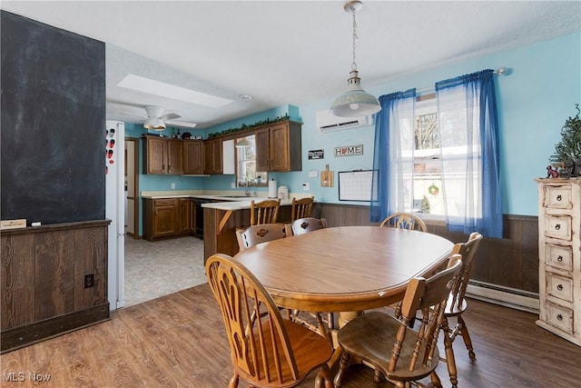 dining room featuring light wood-type flooring, ceiling fan, a wall mounted air conditioner, a baseboard heating unit, and sink