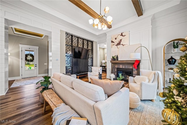 living room with hardwood / wood-style floors, crown molding, beamed ceiling, a notable chandelier, and a brick fireplace