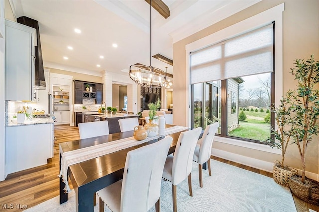 dining space with light wood-type flooring, a chandelier, beamed ceiling, and sink