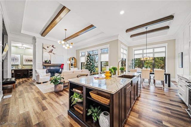 kitchen with dark brown cabinetry, wood-type flooring, hanging light fixtures, light stone countertops, and a center island with sink