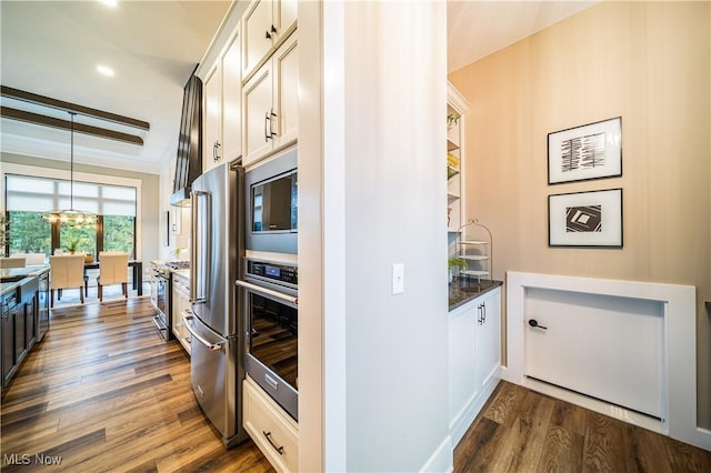 kitchen with dark wood-type flooring, pendant lighting, stainless steel appliances, white cabinets, and beamed ceiling