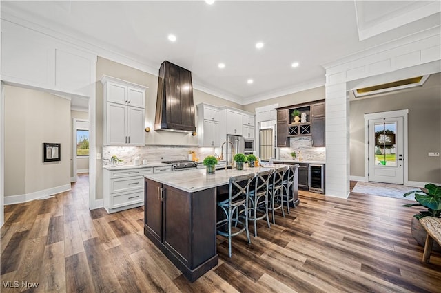 kitchen featuring a healthy amount of sunlight, a kitchen bar, a center island with sink, and premium range hood