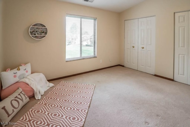 bedroom featuring two closets, light colored carpet, and lofted ceiling