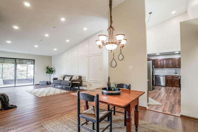 dining area featuring a notable chandelier, high vaulted ceiling, sink, and hardwood / wood-style flooring