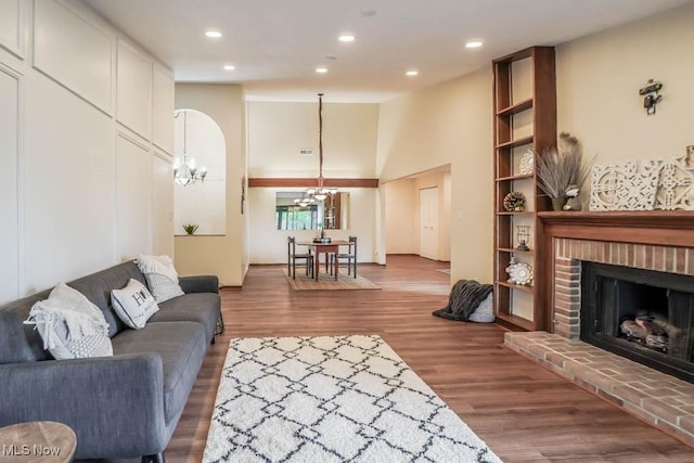 living room featuring a high ceiling, a brick fireplace, an inviting chandelier, and hardwood / wood-style floors