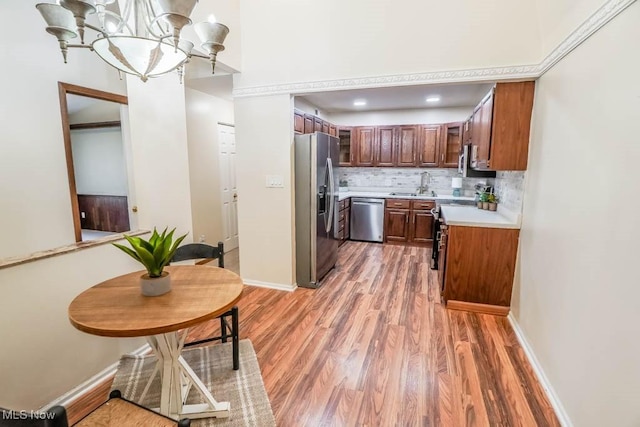 kitchen with wood-type flooring, stainless steel appliances, sink, an inviting chandelier, and tasteful backsplash