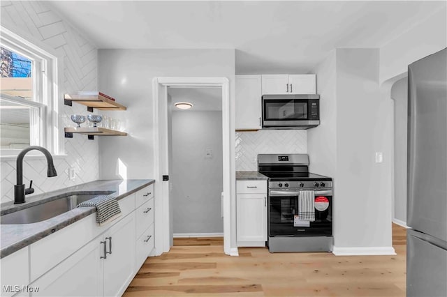 kitchen with sink, white cabinetry, light wood-type flooring, decorative backsplash, and appliances with stainless steel finishes