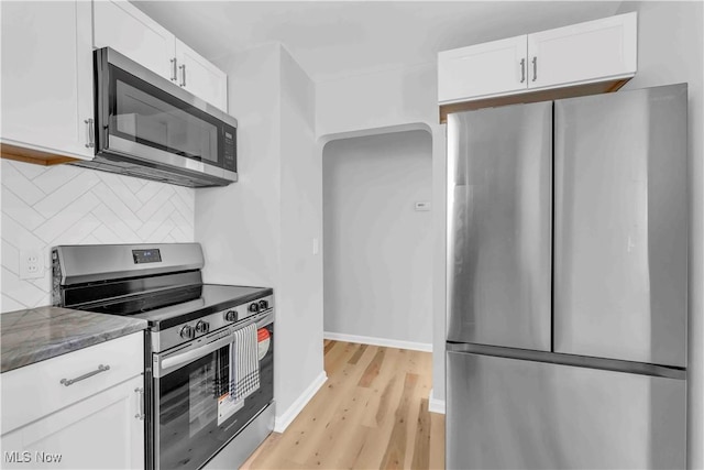 kitchen with stainless steel appliances, dark stone countertops, backsplash, and white cabinetry