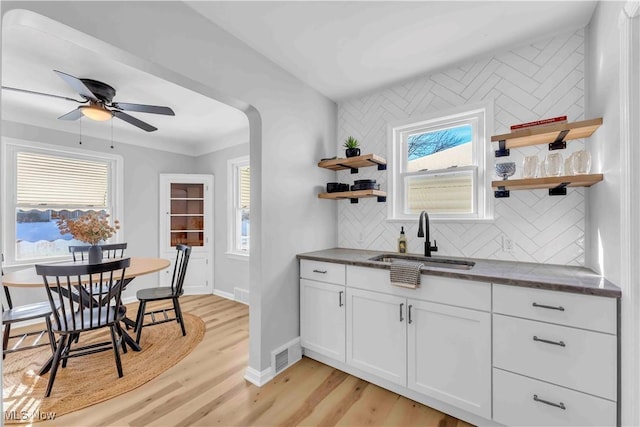 kitchen with sink, white cabinets, ceiling fan, light hardwood / wood-style flooring, and decorative backsplash