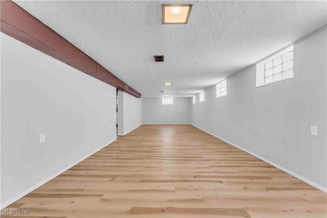 basement with light hardwood / wood-style floors, wood walls, and a textured ceiling