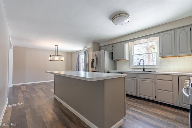 kitchen with stainless steel fridge with ice dispenser, hanging light fixtures, a wealth of natural light, a kitchen island, and sink